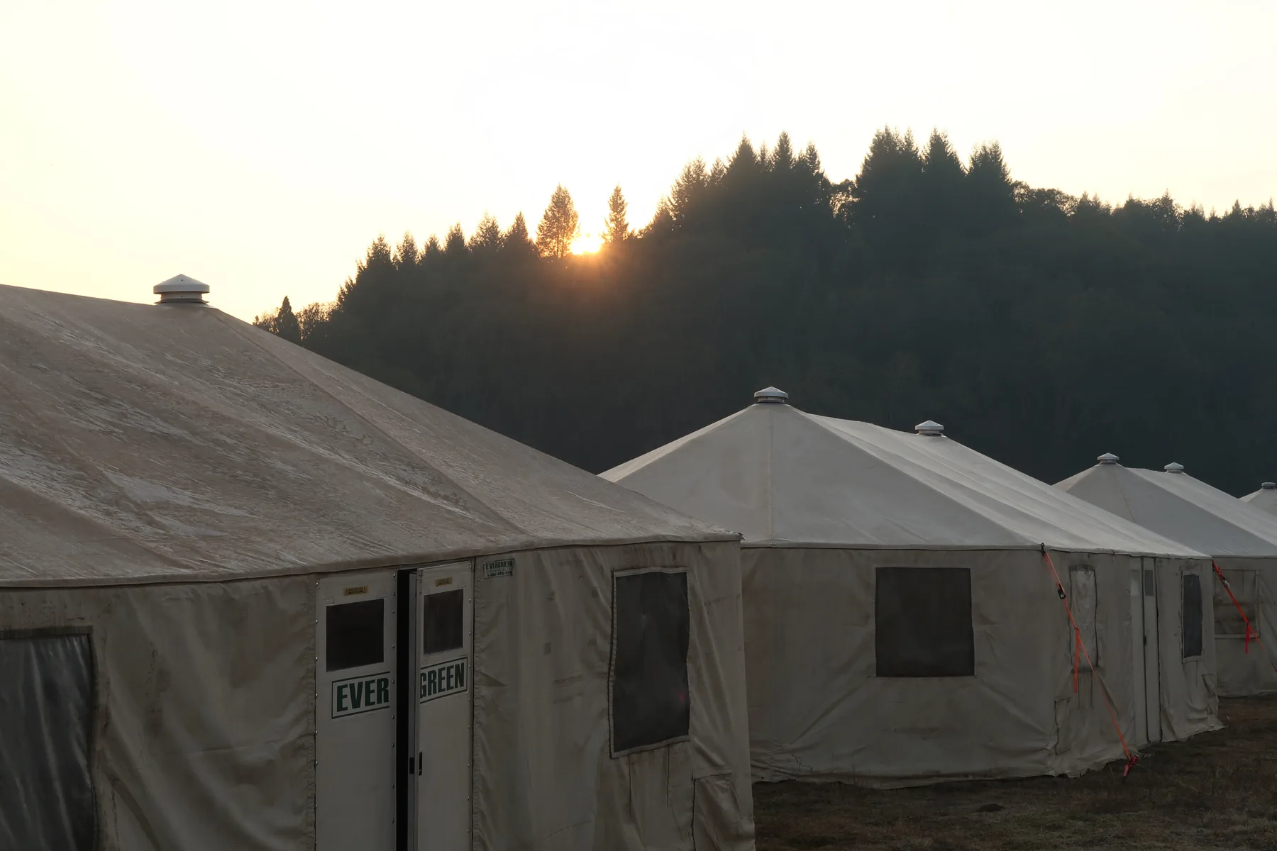 A row of Evergreen Resource yurts at golden hour with the sun behind the ridge